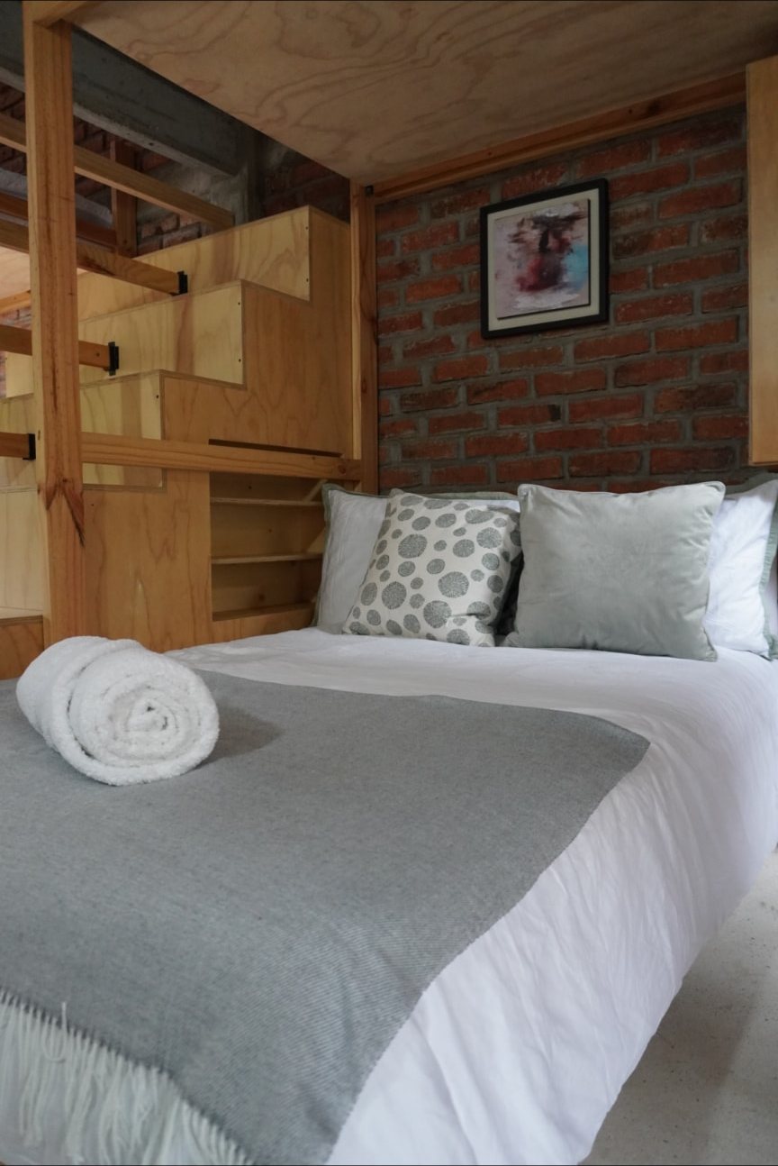 Cama tendida con mantas grises y toallas en Wailele