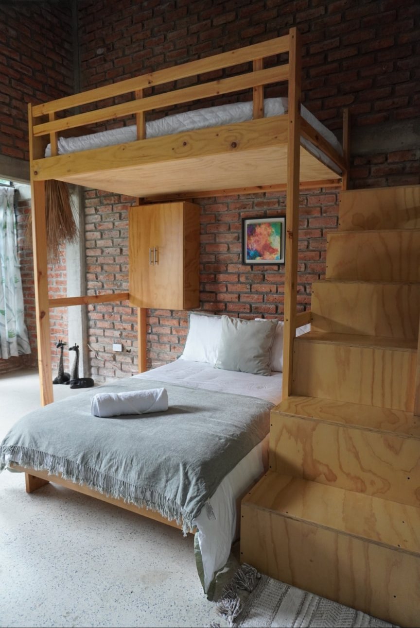 Habitación con cama doble y litera en madera sobre muro de ladrillo